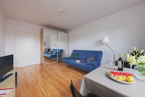 A modern living room with a blue sofa, a dining table with a plate of fruit, a wine bottle, and a vase of flowers. - P&O Apartments Namyslowska (Warsaw)