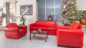 Un vestíbulo con sofás de cuero rojo, una mesa de centro, un muro de piedra con plantas, un cuadro enmarcado y una escalera.