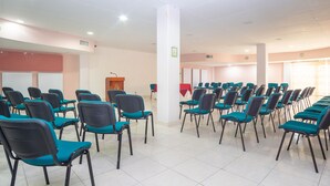 Un salón de conferencias con filas de sillas color turquesa y un atril.