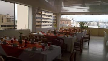 Un restaurante con varias mesas dispuestas para comer, vistas de la ciudad a través de amplios ventanales y una zona de balcón.