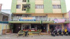 Un edificio de varios pisos con fachada verde y beige, un cartel que indica 'Hotel Sulicam' y varias motocicletas estacionadas en la parte delantera.