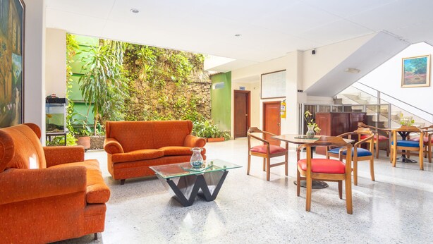 Un vestíbulo espacioso con un sofá moderno color naranja, una mesa de centro de vidrio y sillas de madera con cojines de colores.