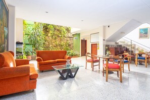 Un vestíbulo espacioso con un sofá moderno color naranja, una mesa de centro de vidrio y sillas de madera con cojines de colores.