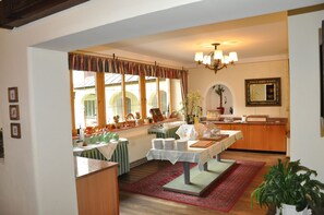 A dining area with a table set for a meal, a chandelier, and a view of the outside through large windows. - Hotel Post (Grosskirchheim)
