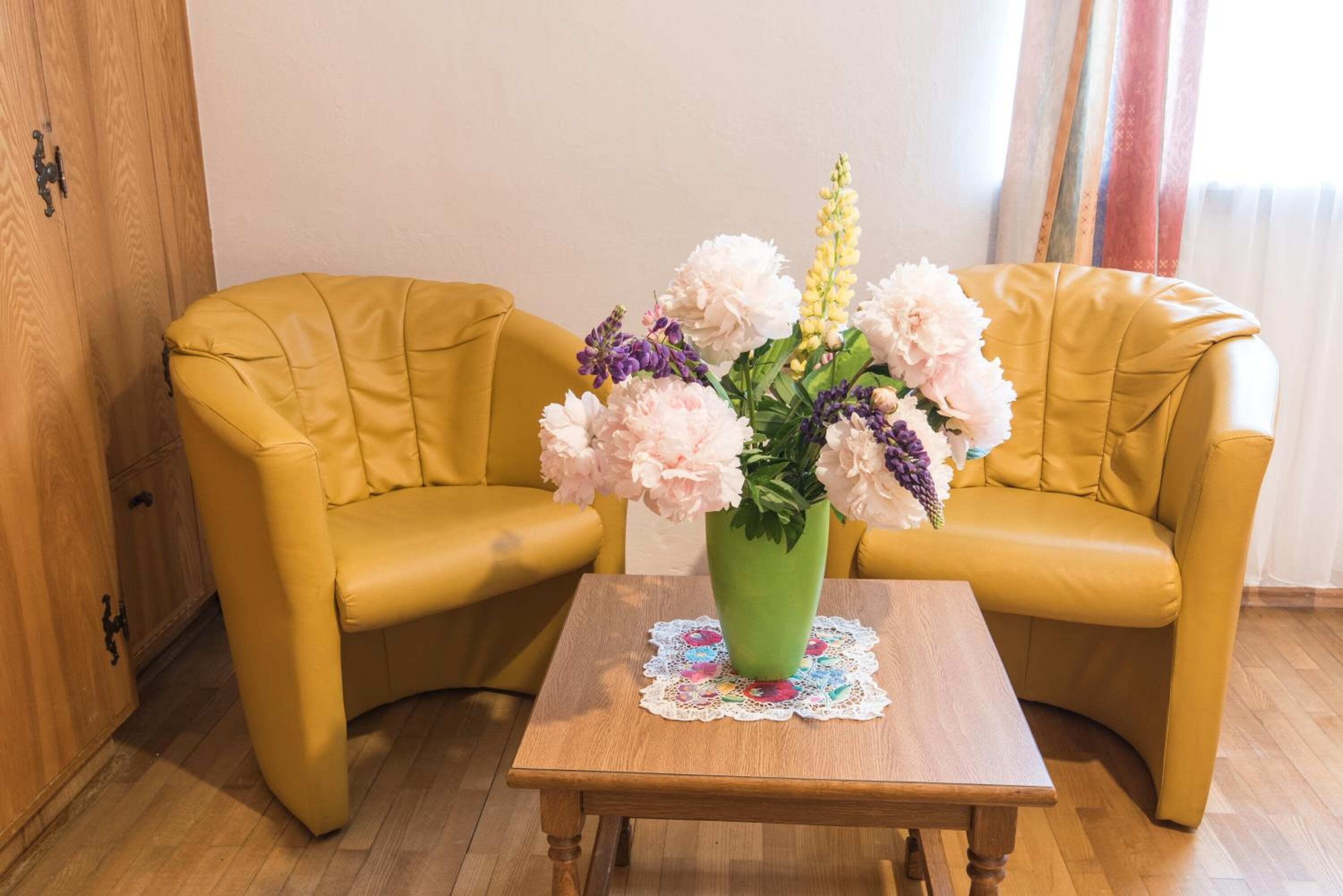 A room with two yellow armchairs, a wooden coffee table, and a green vase with flowers.