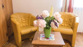 A room with two yellow armchairs, a wooden coffee table, and a green vase with flowers.