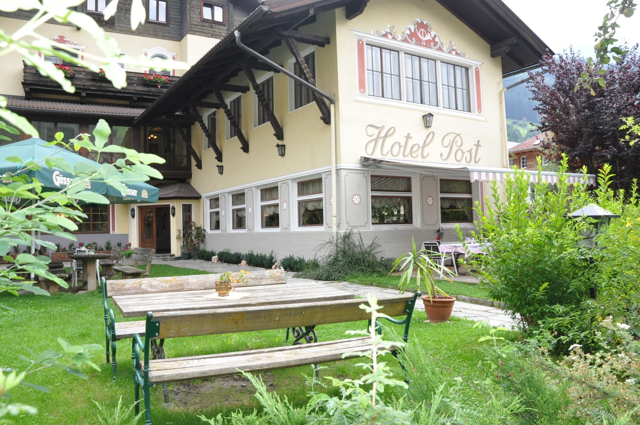 A hotel named "Hotel Post" with a traditional exterior, a garden area with a wooden bench, and outdoor seating.