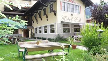 A hotel named "Hotel Post" with a traditional exterior, a garden area with a wooden bench, and outdoor seating.