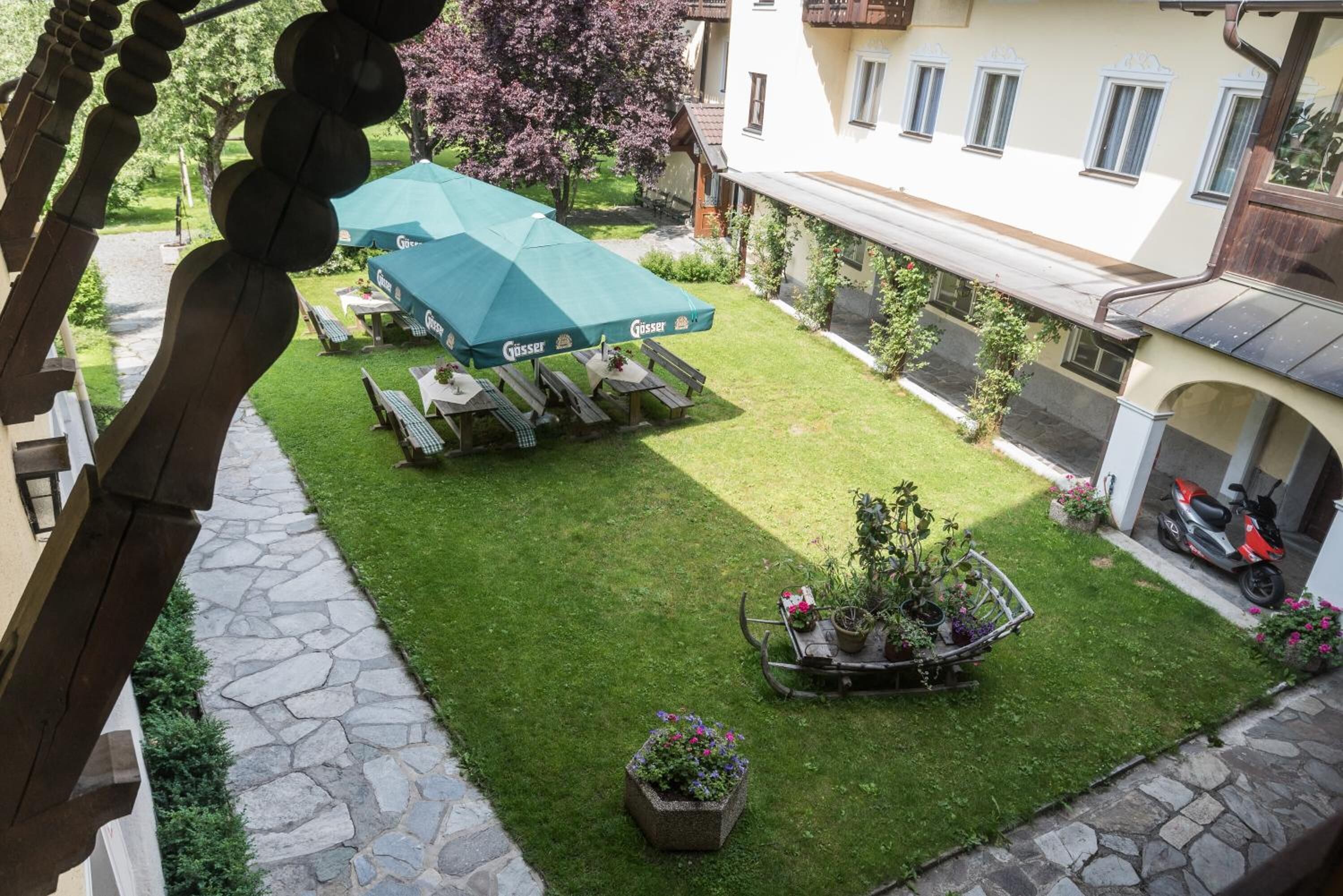 A courtyard with a green lawn, outdoor seating, and a garden cart with potted plants.