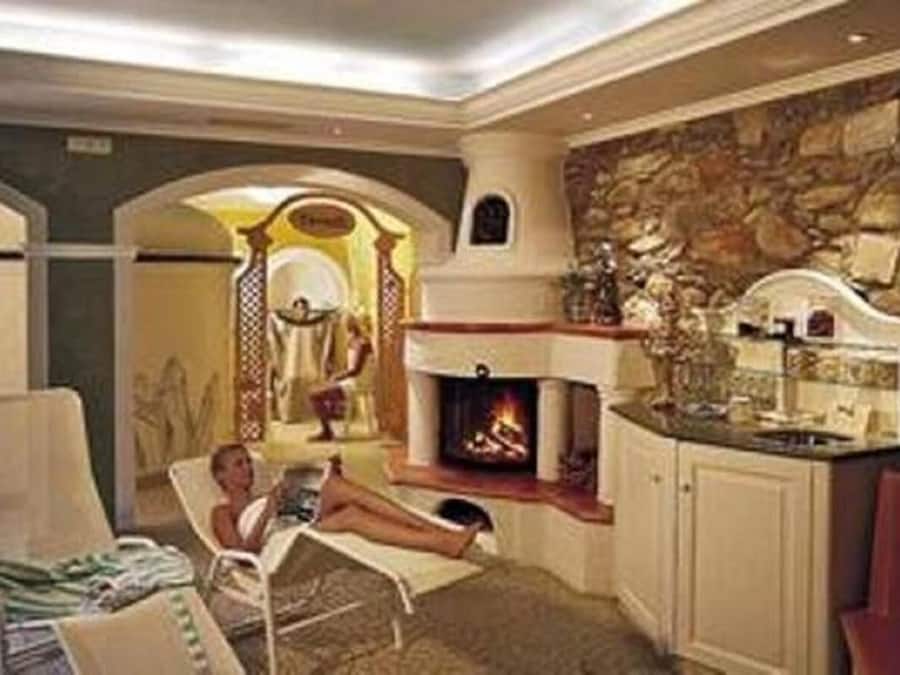 A cozy living room with a fireplace, a stone wall, and a woman relaxing on a chair.