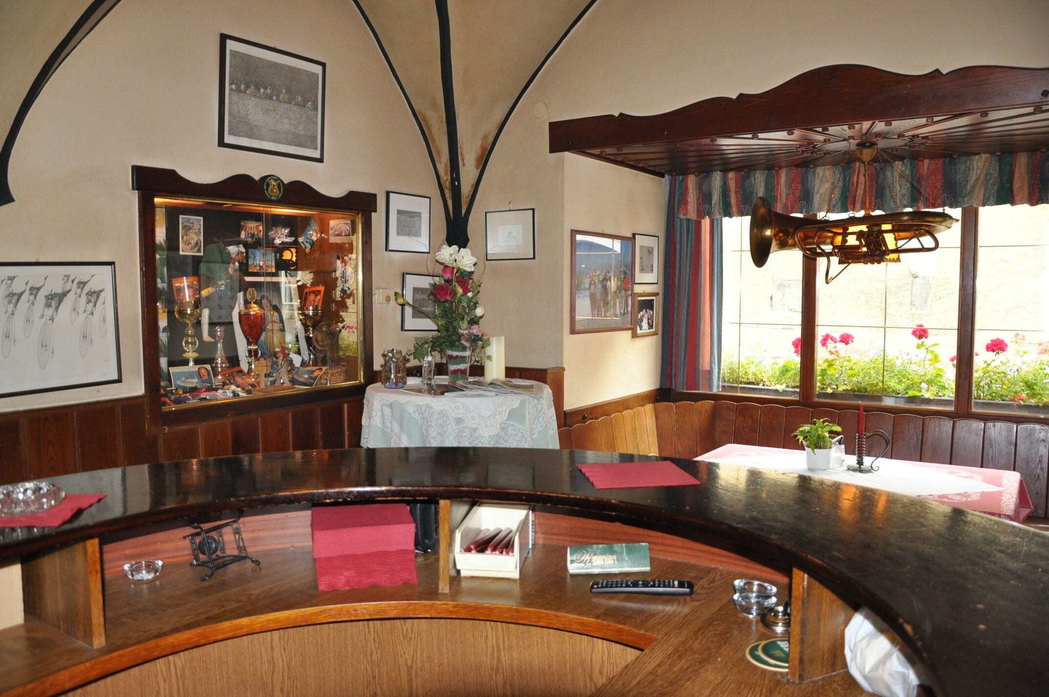Eine Bar mit einer gebogenen Theke, gerahmten Bildern an den Wänden und einem Fenster mit Blick auf Blumen.