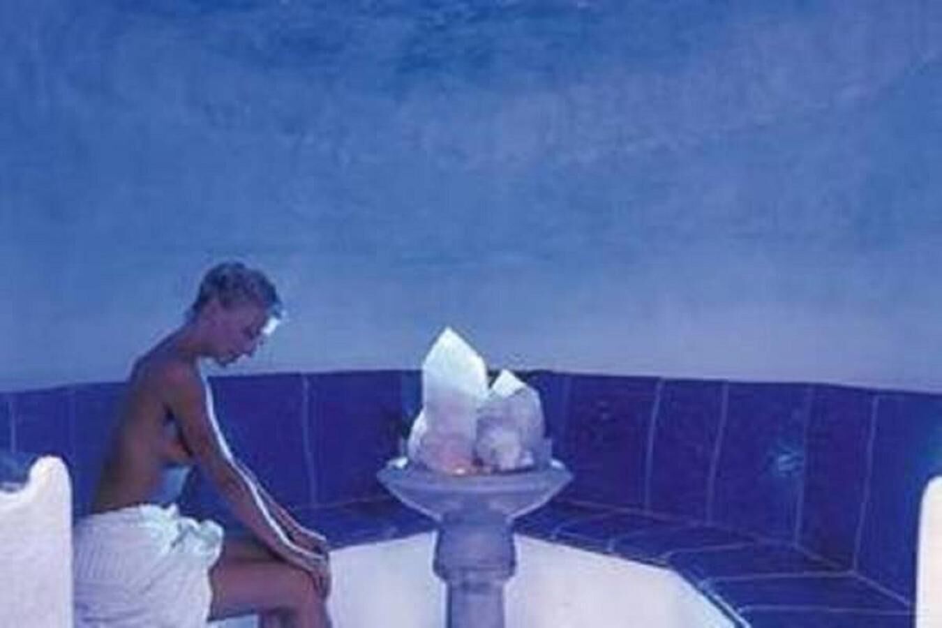A person sitting by a blue-tiled bathtub with a white towel.