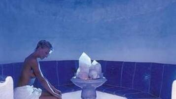 A person sitting by a blue-tiled bathtub with a white towel.