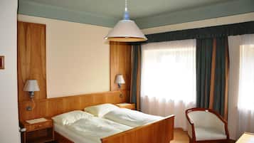 A hotel room with a wooden bed, two bedside tables with lamps, a chair, and a window with curtains.