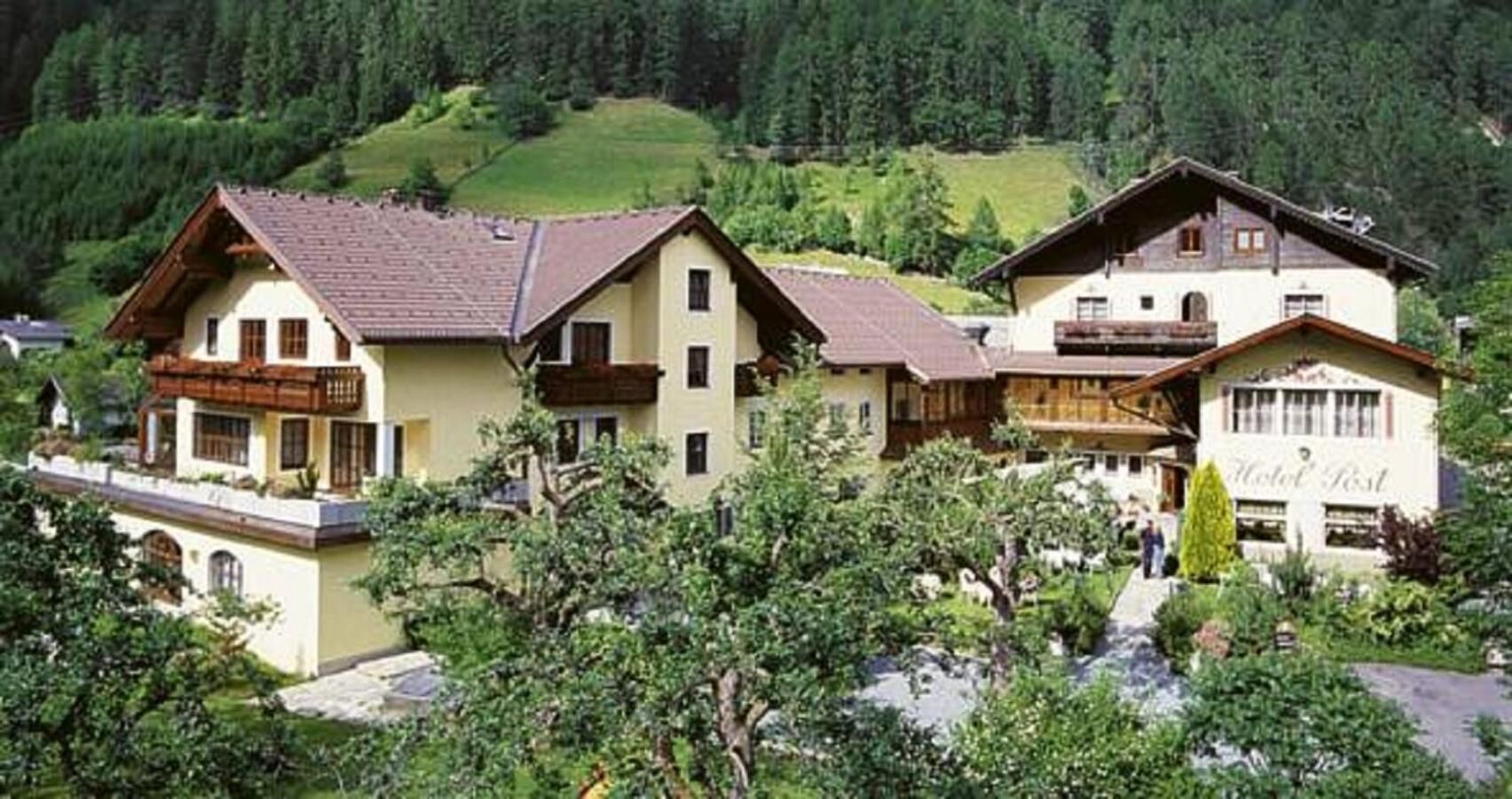 Ein traditionelles Chalet-Hotel mit mehreren Gebäuden, umgeben von üppiger Vegetation und einer Bergkulisse.