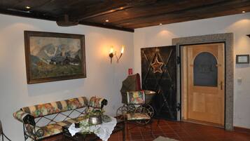 Quarto com um banco de madeira, uma pequena mesa com uma planta, um quadro na parede, uma porta com decoração em forma de estrela e um candeeiro fixado na parede.