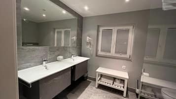 A modern bathroom with a double sink vanity, a bench, and a toilet.