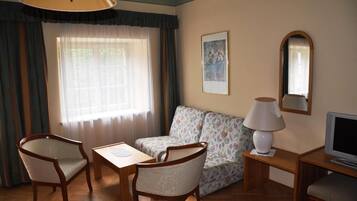 A room with a sofa, two chairs, a table, a lamp, a TV, and a window with curtains.