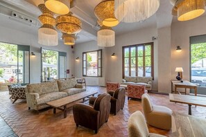 A spacious lobby with multiple seating areas, large windows, and hanging light fixtures. - Hoposa Cultural Boutique (Pollenca)