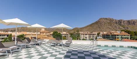 A rooftop pool area with checkered flooring, sun loungers, and umbrellas.