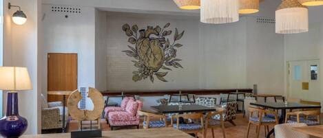 A hotel lobby with a large wall mural, multiple dining tables, and chairs.