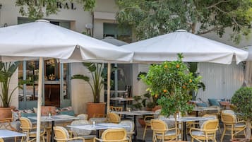 An outdoor café with tables and chairs, surrounded by potted plants and umbrellas.