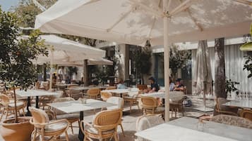 Un café al aire libre con mesas, sillas, sombrillas y plantas en macetas.