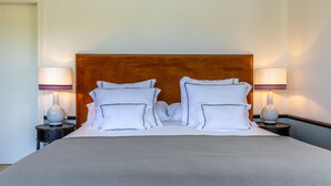A neatly made bed with white linens and pillows, a wooden headboard, and two bedside lamps on matching nightstands. - Hoposa Cultural Boutique (Pollenca)