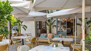 An outdoor cafe with tables and chairs, potted plants, and a stone wall in the background. - Hoposa Cultural Boutique (Pollenca)