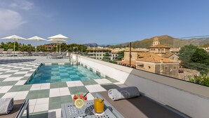 A rooftop pool area with checkered flooring, lounge chairs, umbrellas, and a table with drinks. - Hoposa Cultural Boutique (Pollenca)