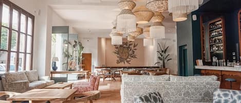 Een ruime zithoek met diverse zitplaatsen, waaronder banken en tafels, en een bar met flessenkasten.