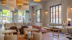 A spacious indoor area with multiple seating options, including sofas and tables, and large windows providing natural light. - Hoposa Cultural Boutique (Pollenca)