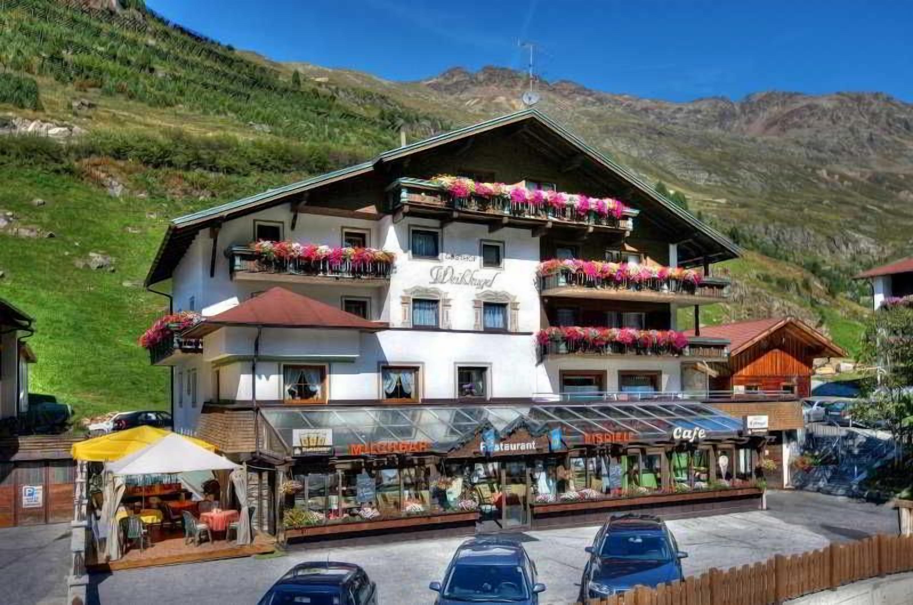 Un edificio de varios pisos con balcones decorados con flores, un restaurante y una cafetería.
