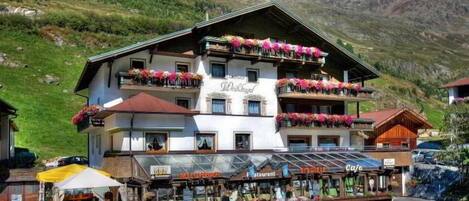 Un edificio de varios pisos con balcones decorados con flores, un restaurante y una cafetería.