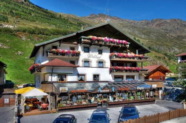 A multi-story hotel with balconies adorned with flowers, a ground-level restaurant, and a parking area.