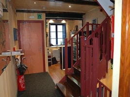 Un pasillo de hotel con una escalera de madera, una puerta que da a una habitación y un radiador al fondo.