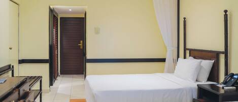 A hotel room with two beds, a wooden nightstand, a desk, and a door leading to another room.