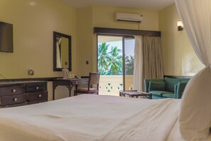 Habitación de hotel con cama, escritorio, silla, sofá verde y balcón con vistas a palmeras.