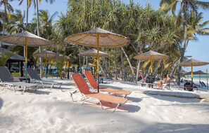 Une plage avec des chaises longues et des parasols en chaume, entourée de palmiers.