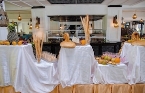 Un buffet disposé sur des tables recouvertes de nappes blanches, avec une variété de fruits, des gressins et des verres remplis de boissons.