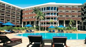 A hotel with a swimming pool, lounge chairs, and umbrellas.