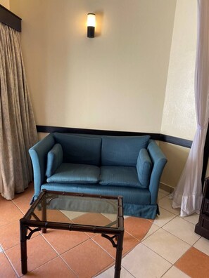 Ein Wohnzimmer mit einem blauen Sofa, einem Glastisch, einer Wandleuchte und einem Vorhang.