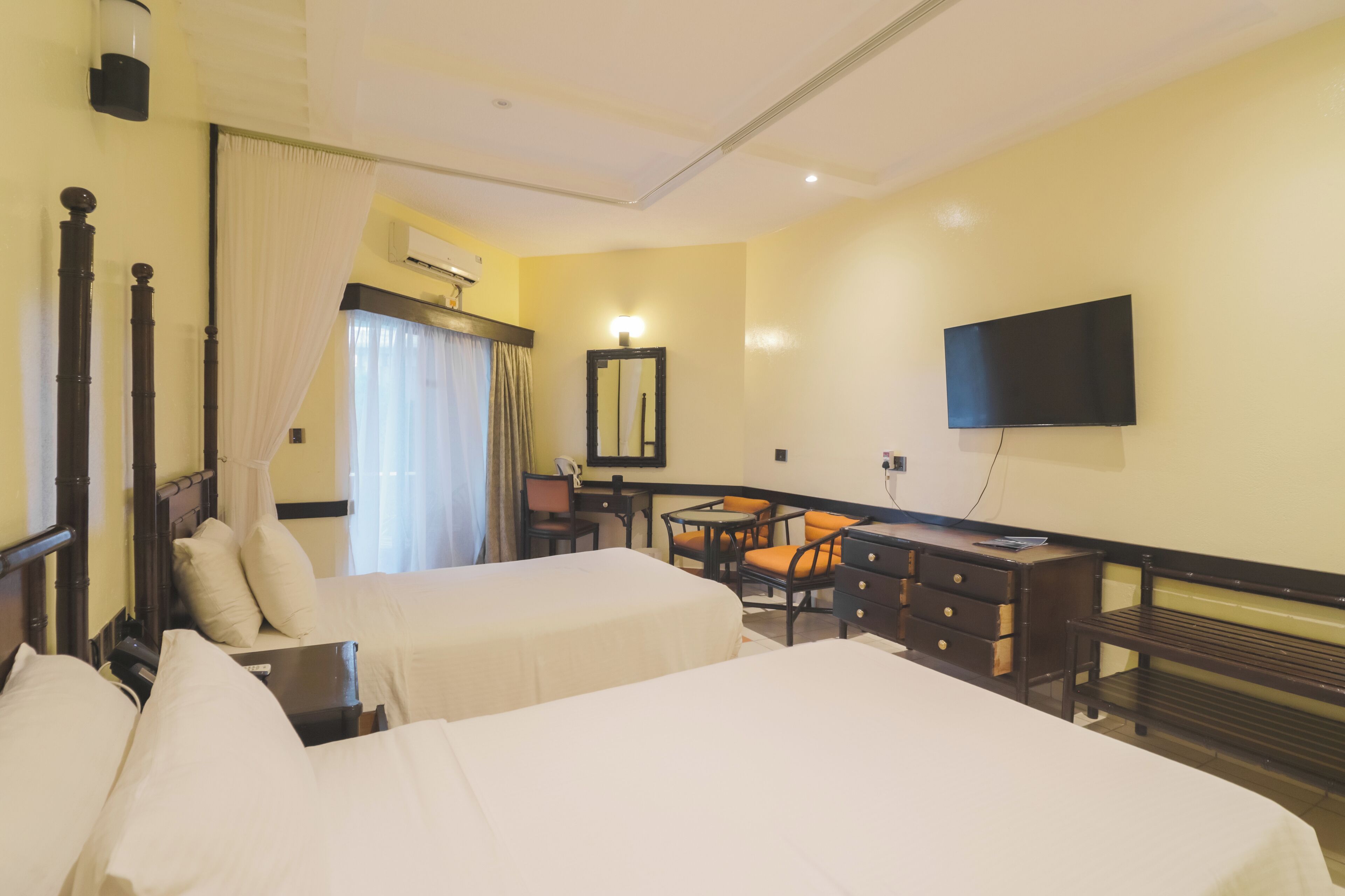 Ein Hotelzimmer mit zwei Betten, einem Schreibtisch, einem Stuhl, einem Fernseher und einem Fenster mit Vorhängen.