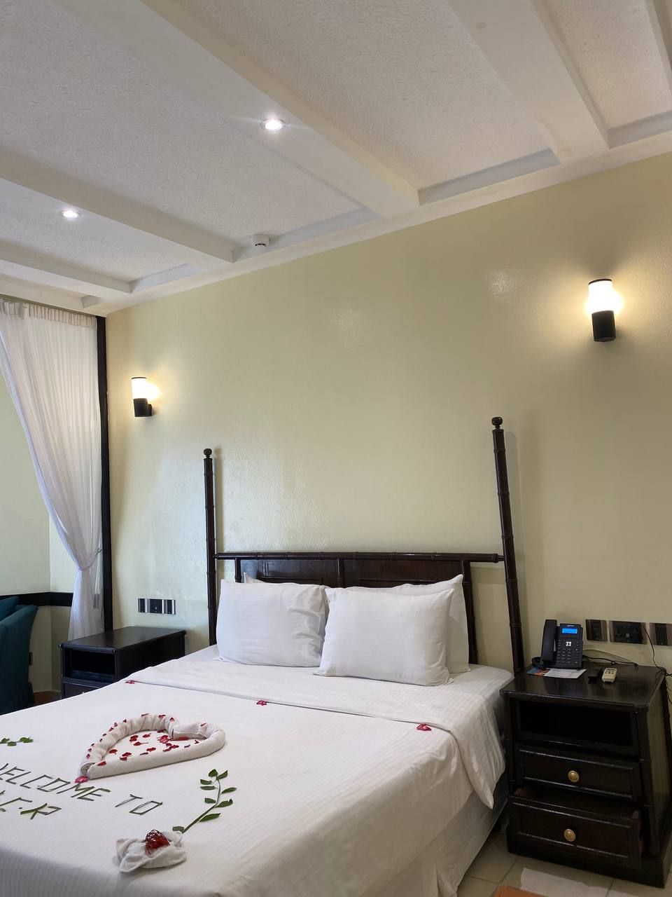 A hotel room with a four-poster bed, a bedside table with a phone, and a wall-mounted light fixture.