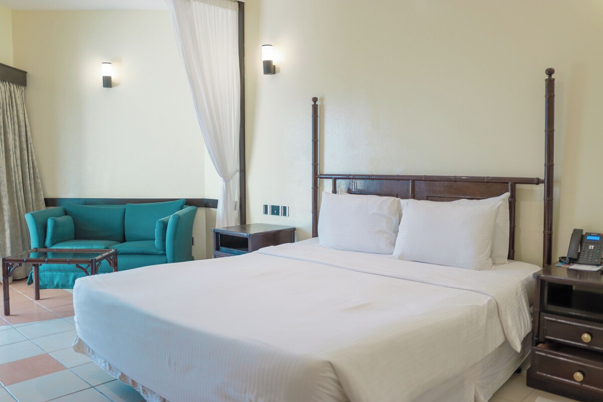 Une chambre d’hôtel avec un grand lit, un canapé de couleur turquoise, une petite table et une table de chevet avec un téléphone.