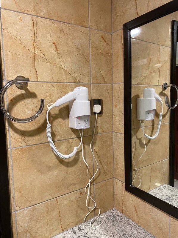 Un baño con un secador de pelo montado en la pared, un aro para toallas y un espejo.