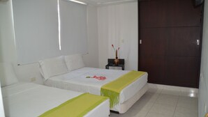 A hotel room with two beds, a small table with a vase, and a dark wooden door.