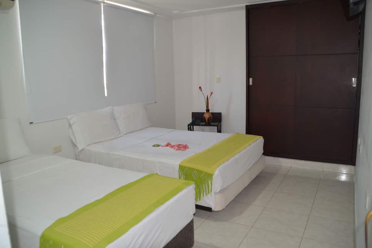 Habitación de hotel con dos camas, una mesita con un florero y una puerta de madera oscura.