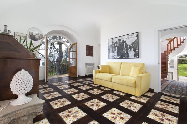 A living room with a yellow sofa, a decorative white sculpture, and a patterned floor. - Capo Santa Fortunata (Sorrento)