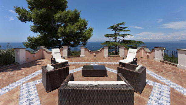 An outdoor patio with wicker furniture, a patterned floor, and a view of the sea. - Capo Santa Fortunata (Sorrento)